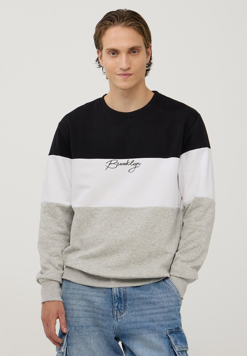 Bluza z kolorowymi blokami w odcieniach czerni, bieli i szarości. Teksturowana bawełna, okrągły dekolt oraz haftowany napis "Brooklyn" na klatce piersiowej.