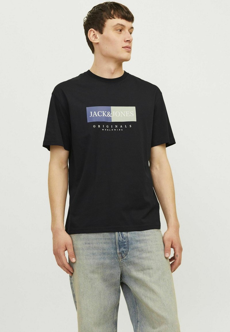 Melna kokvilnas t-kreklā ar daudzkrāsainu grafiku, kurā redzams teksts "JACK&JONES" un "ORIGINALS WORLDWIDE". Īsas piedurknes, apaļa kakla izgriezums.