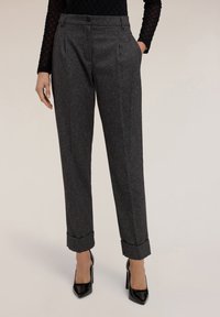 Pantalones grises texturizados con un corte ajustado, pliegues frontales y puños enrollados. Combinados con zapatos de tacón negro.