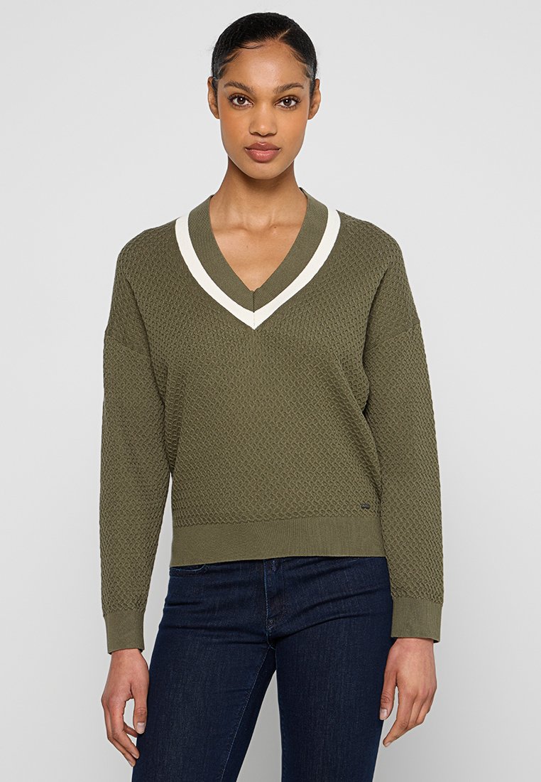 Pull en maille vert olive avec un motif texturé, décolleté en V et bordures blanches. Coupe ample avec des manches longues et un ourlet côtelé.