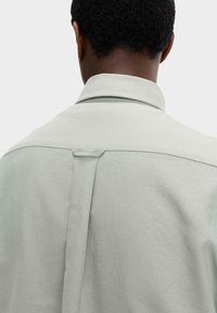 Camicia color grigio chiaro con colletto, caratterizzata da una piega sul retro, una texture liscia e linee pulite, progettata per una vestibilità comoda.