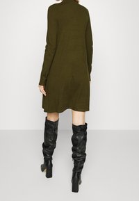 Knelång, olivgrön sweaterklänning med långa ärmar och en avslappnad passform; kombinerad med figursydda svarta läderstövlar som går upp till knäet.