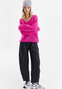 Pulover pufoasă, roz aprins, cu decolteu în V și mâneci lungi, asortată cu pantaloni negri cu dungi subțiri. Căciulă gri tricotată și adidași albi.