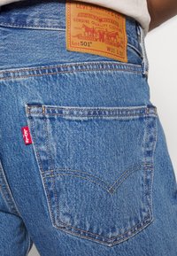 Jean Levi's 501 bleu avec poche arrière visible et patch en cuir marron indiquant la taille W31 L32.