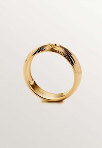 Anillo de oro con una superficie lisa y pulida y detalles texturizados en la parte frontal, que presenta surcos verticales que irradian desde un punto central.