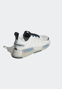 Vitt sportigt sneakers med svarta snören, texturerad ovandel och blå accenter. Har en vadderad sula och ett mönstrat hälstöd för extra st öd.