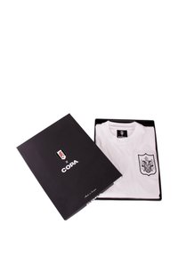 Witte T-shirt in een zwarte doos, met een schildontwerp op de zak. De doos heeft een logo-graphic en "COPA" in witte tekst.