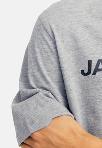 Grau Baumwoll-T-Shirt mit kurzen Ärmeln und umgeschlagenem Saum, mit dunkel gefärbtem Aufdruck auf der Vorderseite und einer glatten, weichen Textur.