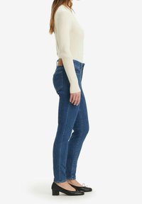 Suéter de crema con canalé combinado con jeans de mezclilla azul oscuro y bailarinas negras con tacón. Una vista lateral resalta el diseño ajustado y la textura.