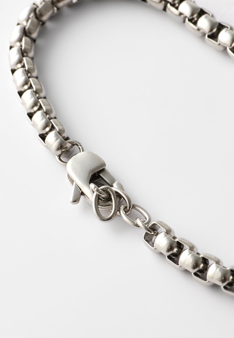 Chaîne en métal argenté avec des maillons ronds et un fermoir à lobster. Texture lisse avec un fini poli et des détails matériels visibles.