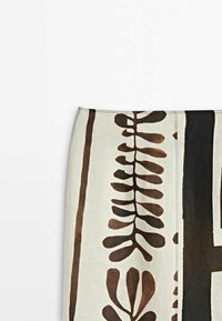 Stof met een beige achtergrond met grote bruine bladdessins. Het materiaal heeft een gladde textuur en vertoont zichtbaar stikwerk langs de randen.