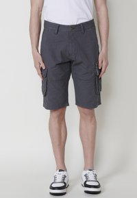 Grijze cargoshorts met zijzakken, gemaakt van lichte stof, met een ontspannen pasvorm en knielange snit, gecombineerd met zwart-witte sneakers.