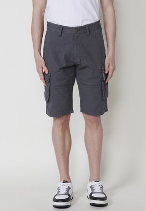 Grijze cargoshorts met zijzakken, gemaakt van lichte stof, met een ontspannen pasvorm en knielange snit, gecombineerd met zwart-witte sneakers.
