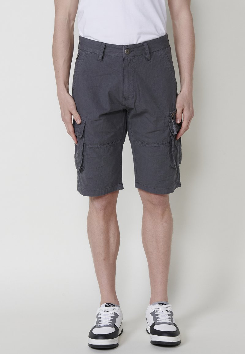 Grijze cargoshorts met zijzakken, gemaakt van lichte stof, met een ontspannen pasvorm en knielange snit, gecombineerd met zwart-witte sneakers.