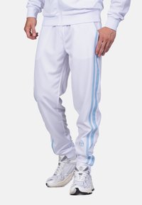 Weiße Sporthosen mit zwei hellblauen Seitenstreifen, einem Kordelzugbund und einem Logo auf dem linken Bein. Hergestellt aus einem glatten, atmungsaktiven Material.