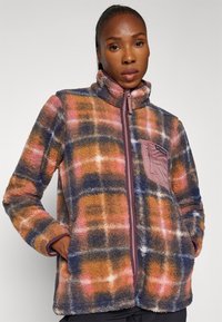 Giacca in pile con zip, caratterizzata da un motivo a quadri in arancioni, blu e rosa. Include una tasca sul petto e colletto alto.