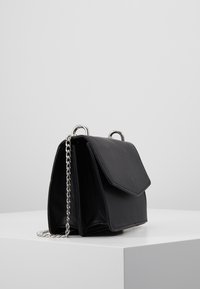 Borsa a tracolla nera in pelle con forma strutturata, dotata di chiusura a patta e tracolla in catena argentata. Texture liscia e design minimalista.