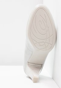 Chaussure à talon aiguille gris clair avec un dessus en daim texturé, un talon carré à motifs et une semelle blanche lisse avec un design de bande de roulement décoratif.