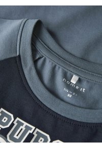 Ciemnoniebieska i szaro-niebieska koszulka z okrągłym dekoltem, z wyraźnym białym napisem. Wykonana z mieszanki bawełny, o gładkiej fakturze i casualowym designie.