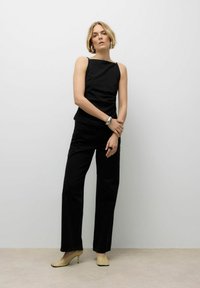 Top nero senza maniche con scollatura quadrata, abbinato a pantaloni neri a gamba larga e tacchi beige. Un bracciale e un anello in argento aggiungono accenti sottili.