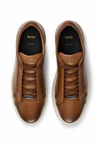 Brązowe skórzane trampki z beżowymi gumowymi podeszwami, z tonowanymi sznurówkami, tłoczonym logo oraz gładkim wykończeniem z subtelnymi detalami szycia.