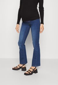 Sininen farkkuhousu, joissa on leveä lahje ja keskikorkea vyötärö, yhdistetty mustiin hihnallisiin paljettikorkokenkiin. Kangas on sileä ja siinä on minimaalista yksityiskohtaisuutta.