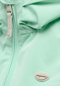 Close-up van muntgroene stof met een ritssluiting en een klein ovaal embleem met de tekst "ragewear" op een gestructureerde outdoorjas.
