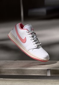 Baskets blanches en cuir avec des accents roses, bout perforé et lacets gris texturés. Elles présentent une semelle en caoutchouc avec des détails roses.