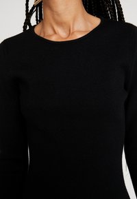 Maglione nero a maglia con scollo rotondo e maniche lunghe; texture liscia senza motivi visibili o dettagli in metallo.
