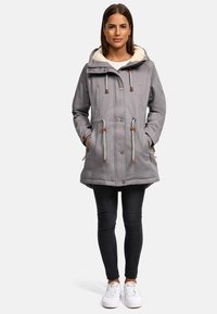 Gray, hooded parka jacket with front button closure, drawstring accents, and fleece lining. Paired with black jeans and white sneakers.