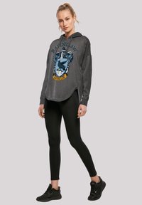 Grå hettegenser med et fronttrykk av Ravenclaw-emblemet, med snor i hetten og sidelommer. Kombinert med svarte leggings og joggesko.