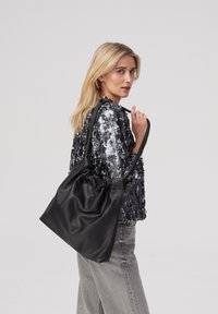 Sort læder tote taske med et samlet design og lange håndtag, der har en glat overflade og minimale hardware detaljer.
