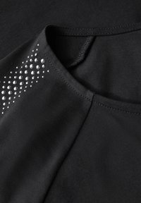 Zwarte stoffen top met een ronde halslijn, met zilveren studs in een gradiëntpatroon op één schouder. Glad oppervlak.