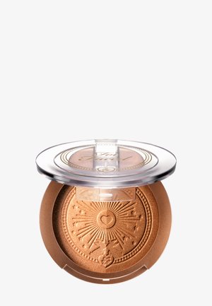 Geöffneter bronzefarbener, gepresster Puderkompakt mit Sonnenstrahlen- und Herzprägung, durchsichtiger Kunststoffdeckel mit goldenem Schriftzug-Logo.