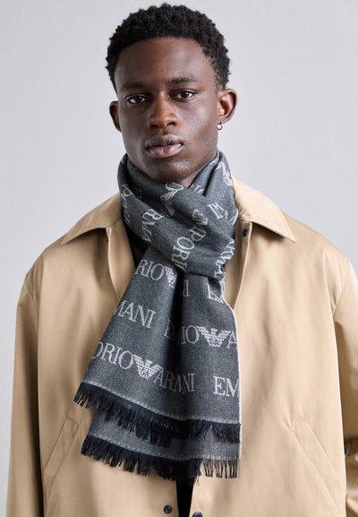 Foulard din lână gri și neagră cu margini franjurate și modele repetitive cu logo-ul "Emporio Armani". Purtați peste o jachetă bej.