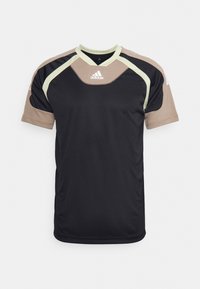 Camiseta atlética negra de manga corta. Acentos en beige claro y verde en los hombros y el cuello. Fabricada con tela transpirable. Logotipo de Adidas visible.