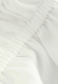 Vitt tyg med en mjuk, texturerad yta och samlingsdetaljer. Ljus och luftig framtoning som framhäver ett delikat vävningsmönster.