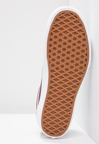 Suola di sneaker con base in gomma marrone a motivo, bordata da un lato bianco. Il design è piatto con una trama a diamante per la presa.