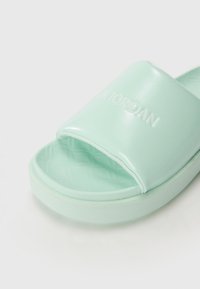 Mint green slide sandal with a glossy texture, featuring a wide strap embossed with "AIR JORDAN" and a contoured sole.