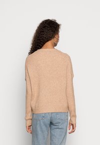 Beżowy sweter dzianinowy o prążkowanej strukturze, w luźnym kroju i z rękawami raglanowymi. W zestawie z jasnoniebieskimi spodniami typu straight-leg.