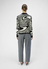 Maglione a spirale in bianco e nero realizzato in tessuto a maglia, abbinato a jeans in denim grigi a vita alta, mostrato dalla vista posteriore.