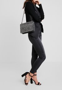 Grå handväska med ormskinnsmönster och kedjesnär, matchad med mörka jeans och svarta högklackade sandaler. Ett övergripande stilrent och modernt utseende.