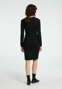 Robe noire ajustée à manches longues avec une taille cintrée et une longueur au genou. Fabriquée en tissu lisse, sans motifs ni embellissements visibles.