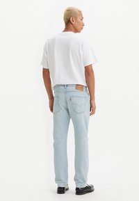 Jeans de mezclilla azul claro con corte recto, con bolsillos traseros, un parche de cuero en la cintura y una camiseta blanca sólida.
