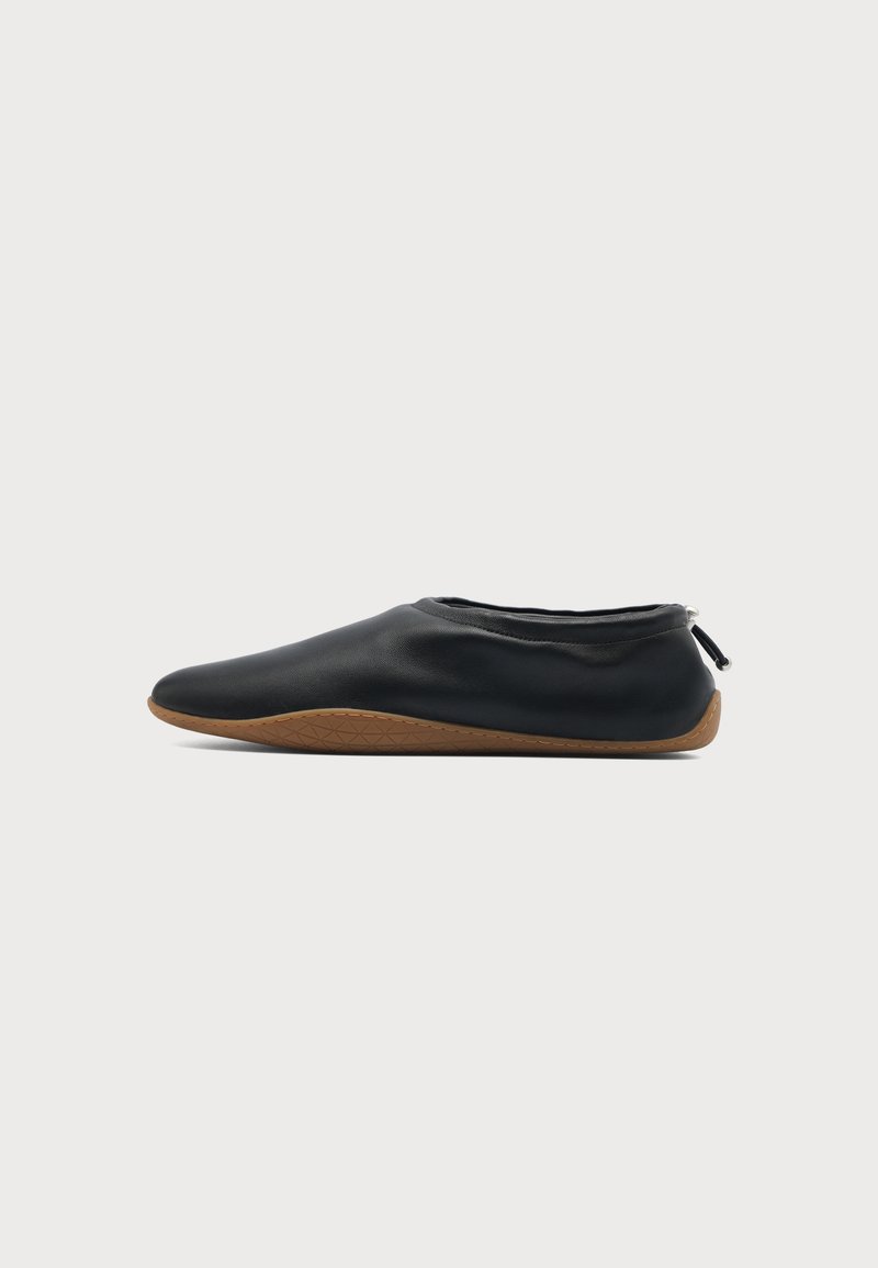 Chaussure plate en cuir souple noir avec semelle en caoutchouc marron et cordon élastique réglable au talon, montrée en profil sur fond blanc.