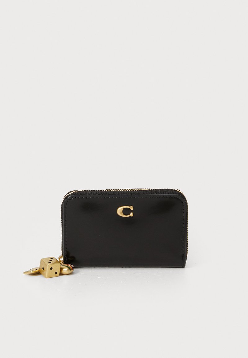 Zwarte leren portemonnee met gouden rits, voorzien van een klein gouden logo en een decoratieve sleutelhanger met dobbelsteen-details. Gladde afwerking en rechthoekige vorm.