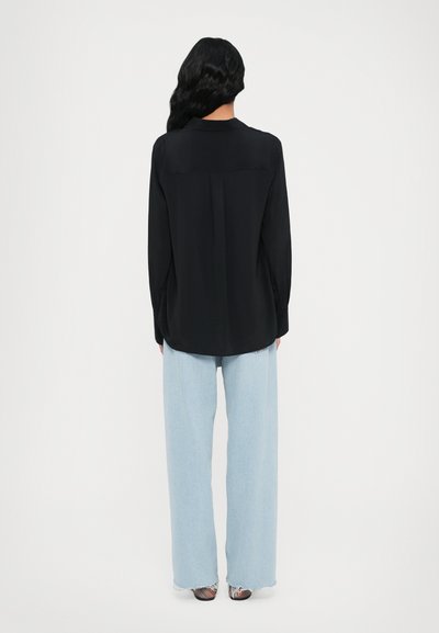 Camisa preta de manga longa com uma textura suave, combinada com jeans de perna larga em azul claro. Os jeans possuem bainhas desfiadas e um ajuste solto.