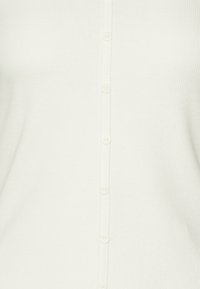 Witte geribbelde cardigan met een rij van zes knopen langs de voorkant, gemaakt van een textuurstof die een subtiel patroon geeft.