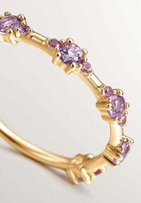 Anillo de oro con múltiples piedras preciosas púrpuras en forma ovalada y redonda, engastadas en garras, con una banda lisa y pulida y acentos texturizados.