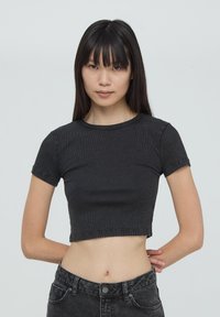 T-shirt nera cropped realizzata in tessuto a coste, con maniche corte e scollo rotondo. Presenta un design aderente e cuciture visibili.